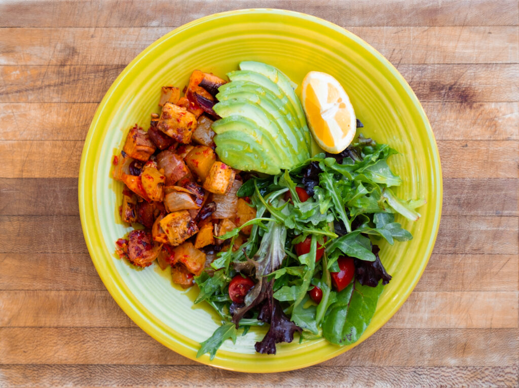 Harissa sweet potatoes and tofu on a bright plate with salad, lemon and avocado.